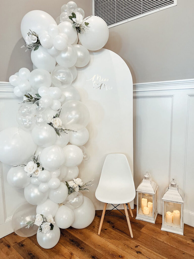 White bridal balloon backdrop with florals and chair for a Luxury Mobile Bar & Balloon Service event.