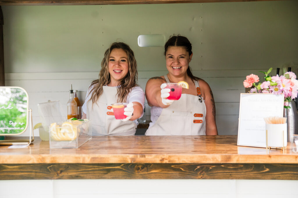Luxury Mobile Bar & Balloon Service bartenders serving pink cocktails from the trailer window.